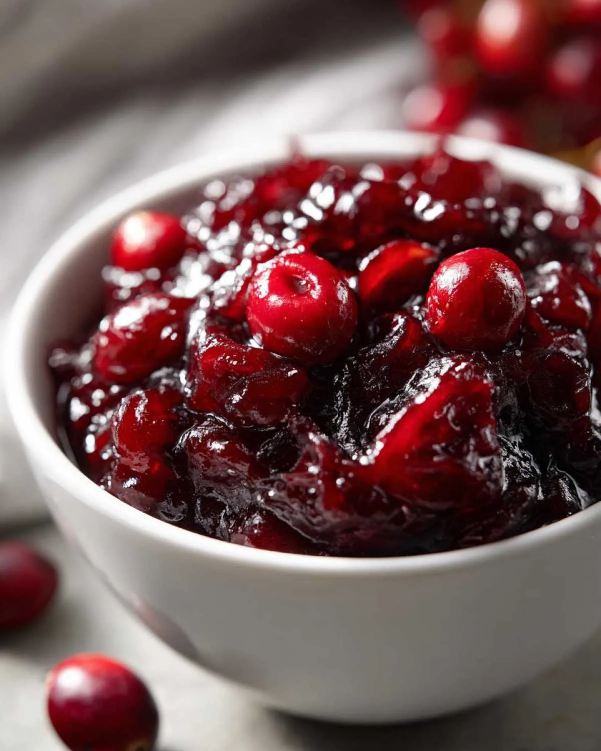 Close-up of a white bowl filled with glistening homemade cranberry sauce, with fresh cranberries scattered around.