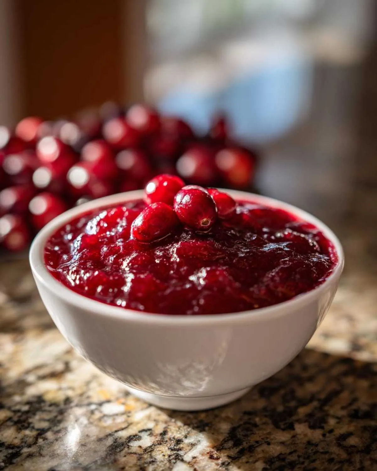 A close-up of a white bowl filled with glistening homemade cranberry sauce, topped with fresh cranberries.