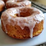 Close-up of a glazed pumpkin donut with cinnamon sprinkles on a white plate. Delicious pumpkin donuts recipe.