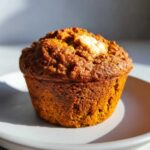 A single keto pumpkin muffin sits on a plate, showcasing its texture and creamy filling.
