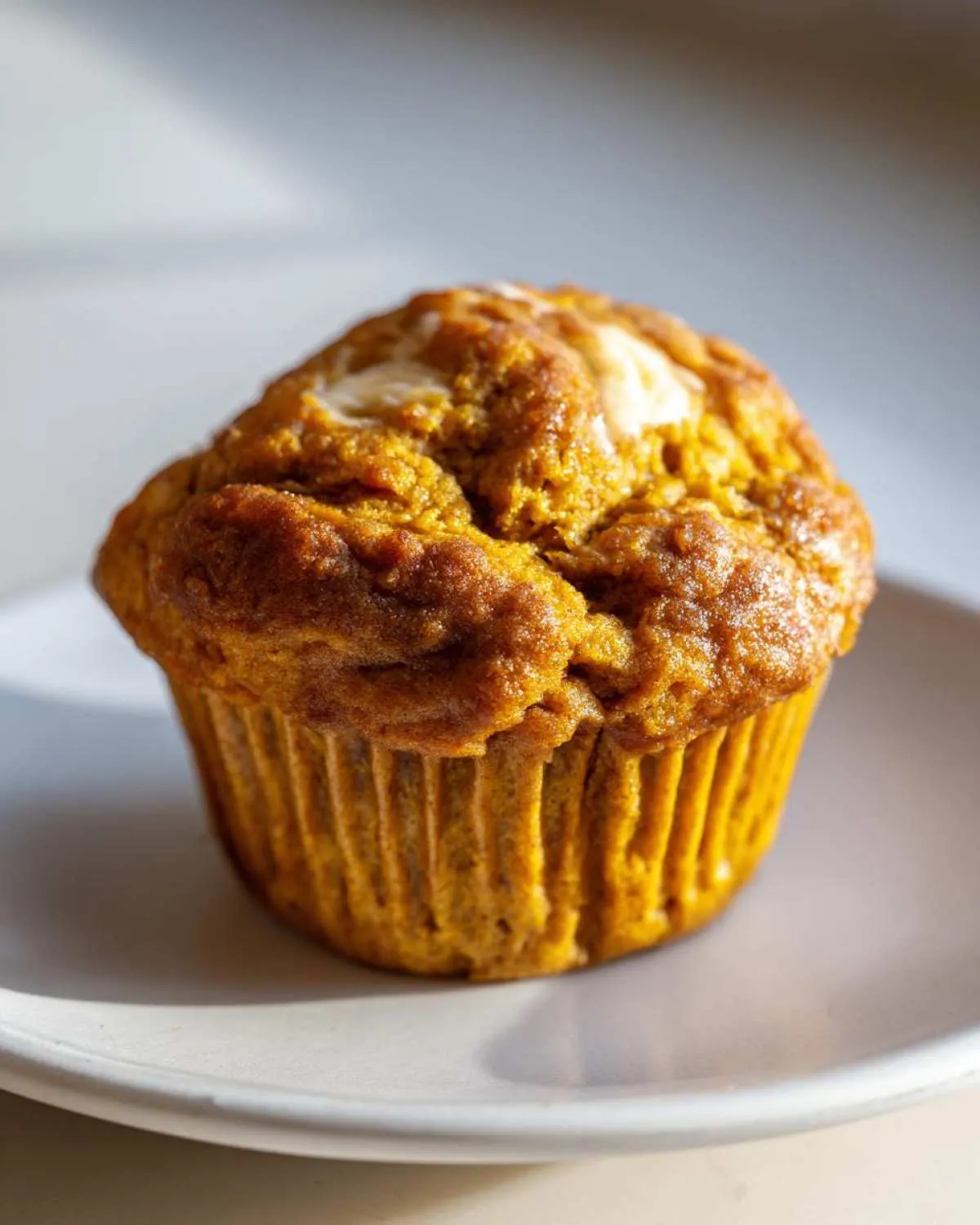 A single keto pumpkin muffin on a white plate, showcasing its texture and color.