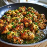 Close-up of golden brown lemon butter chicken pieces sizzling in a pan with lemon zest and parsley.