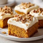 Close-up of moist pumpkin bars topped with cream cheese frosting and chopped nuts.