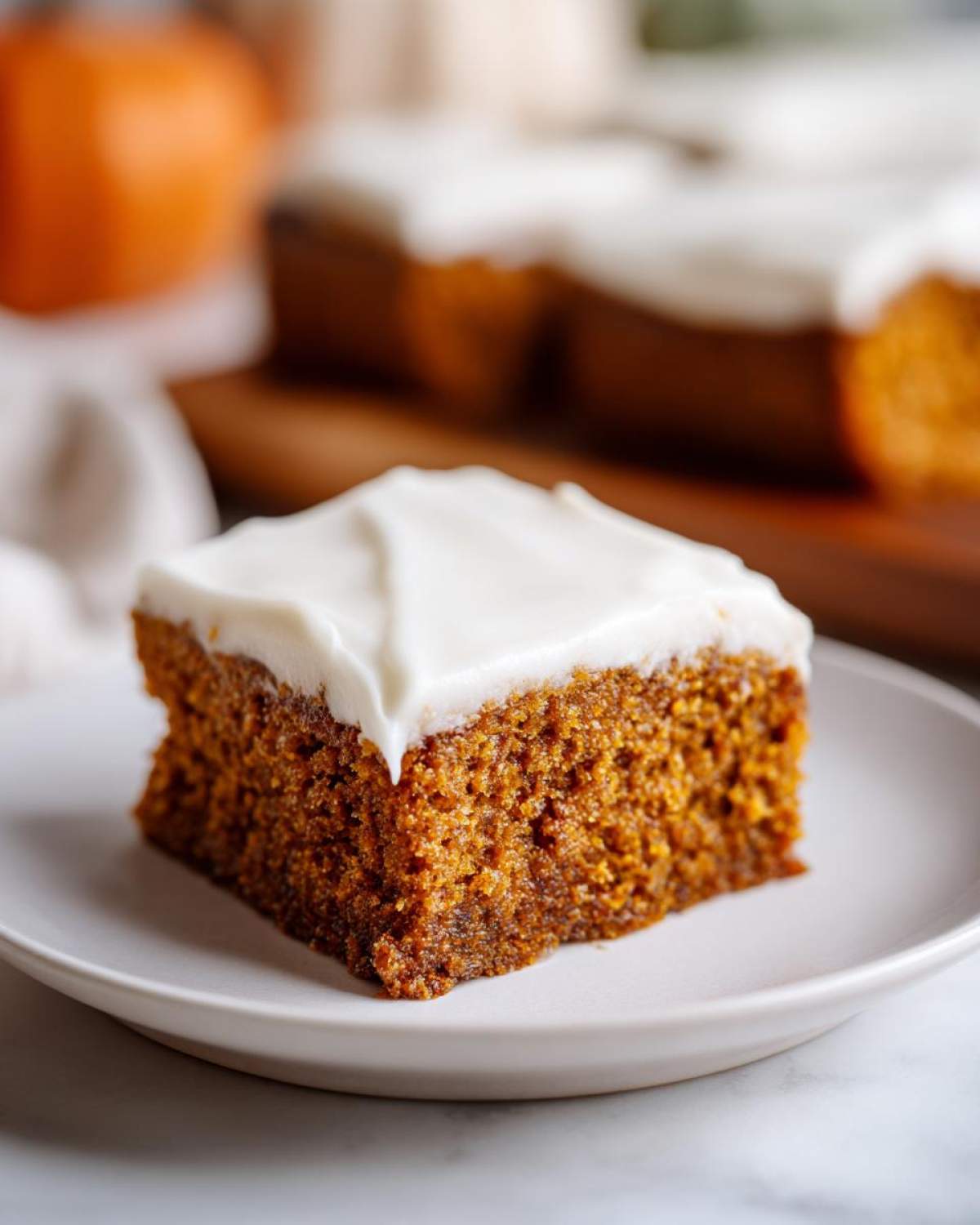 A close-up of a moist pumpkin bar topped with creamy white frosting, ready to be enjoyed.