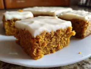 Close-up of moist pumpkin bars topped with creamy white frosting on a white plate.