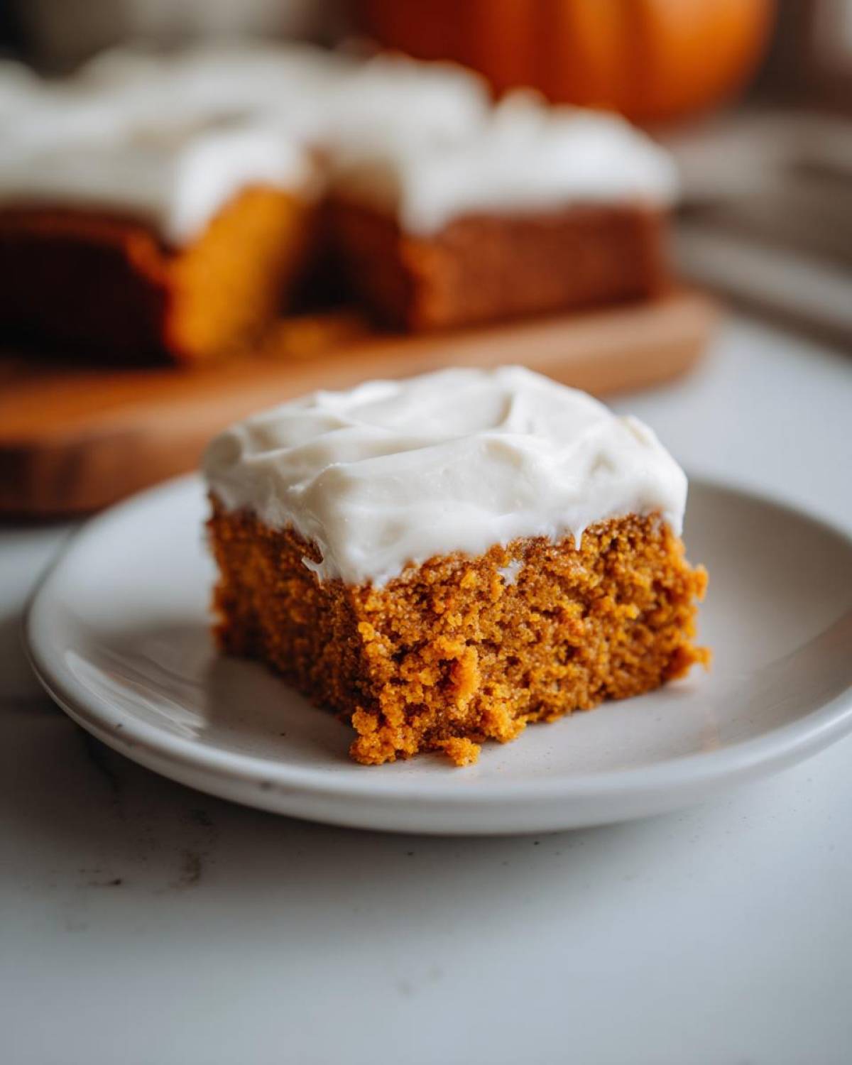 A slice of moist pumpkin bars topped with creamy frosting on a white plate.
