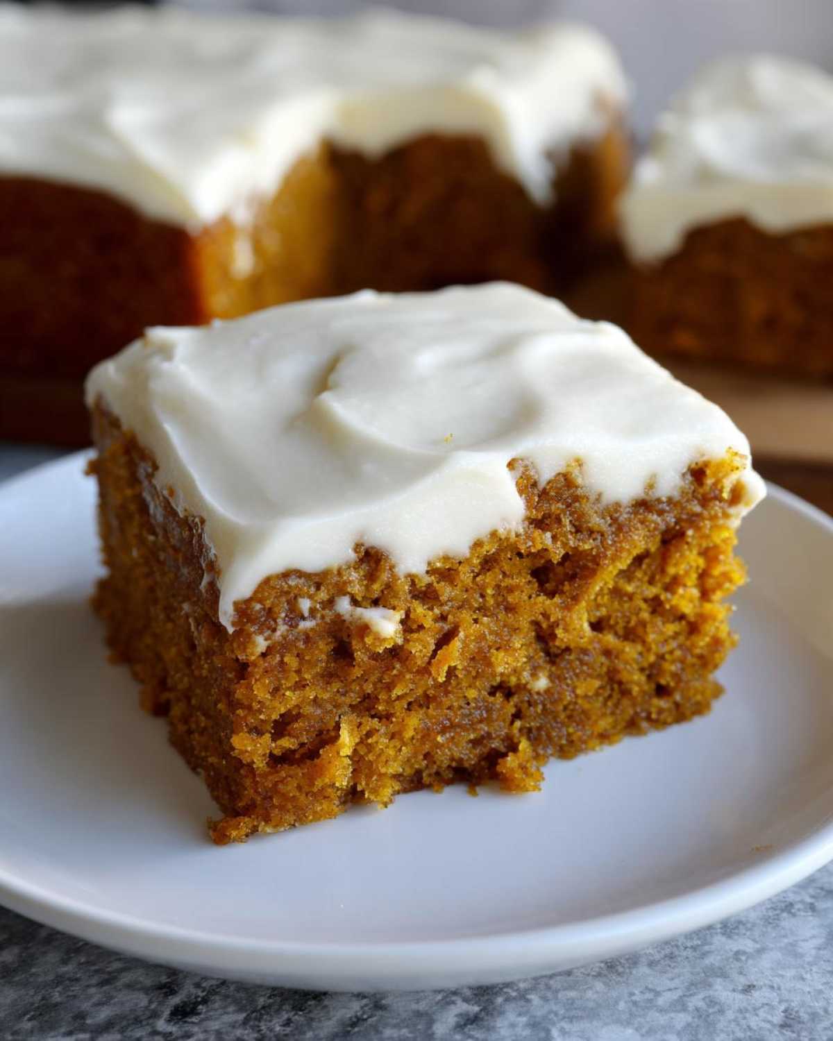 A close-up of a moist pumpkin bar topped with creamy frosting.