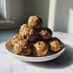 A stack of homemade oatmeal protein balls on a plate, sprinkled with chia seeds and chocolate chips.
