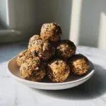 A stack of homemade oatmeal protein balls on a plate, sprinkled with chia seeds and chocolate chips.