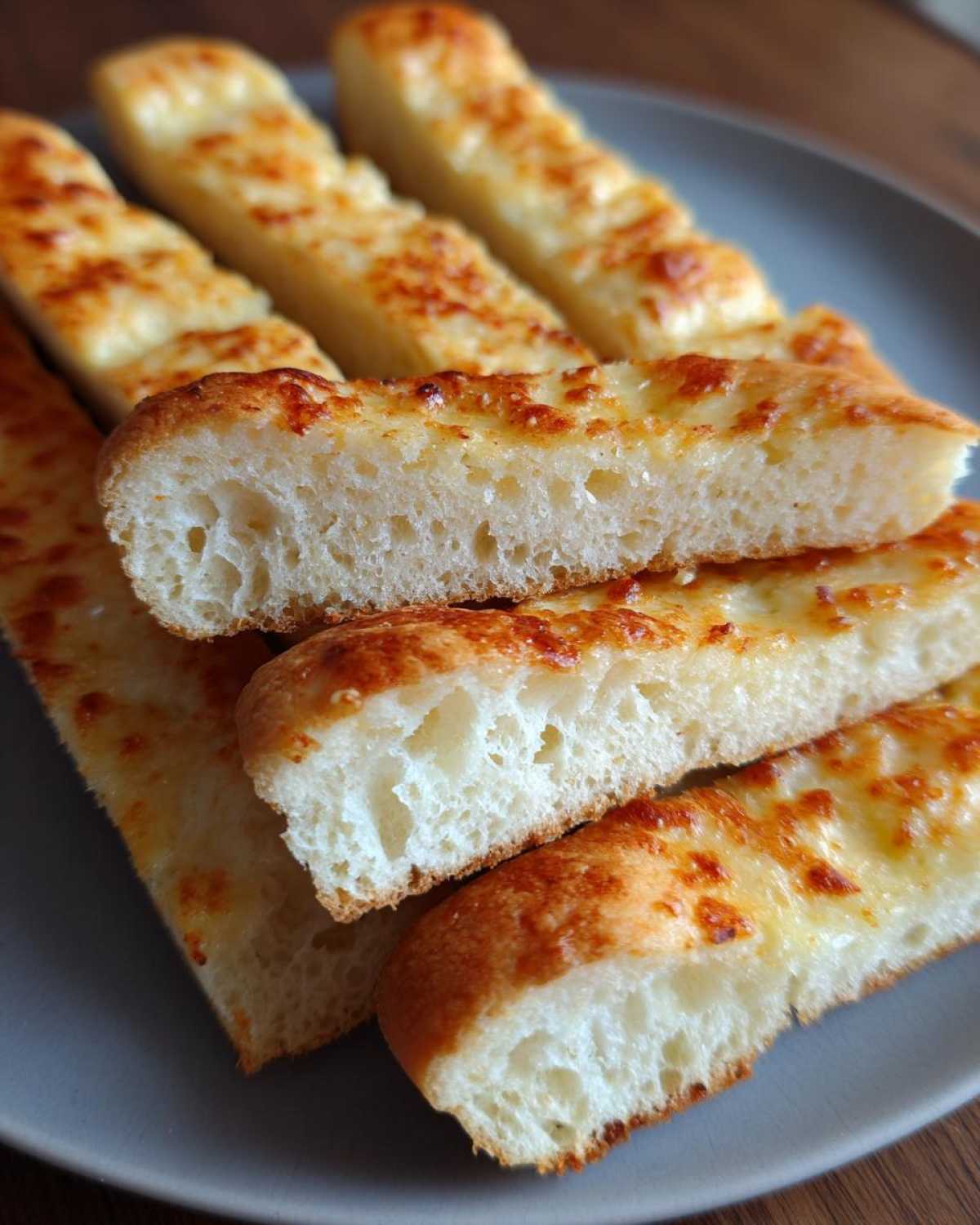 Close-up of soft olive garden breadsticks, golden brown with melted cheese on top, showing a fluffy interior.