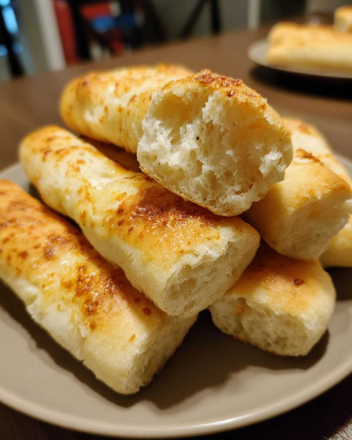 Close-up of golden brown, soft Olive Garden breadsticks piled on a plate, one broken open to show its fluffy interior.