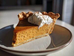 A close-up of a perfect pumpkin pie slice topped with whipped cream and a sprinkle of cinnamon.