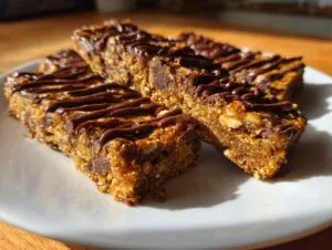 Three homemade protein bars drizzled with chocolate on a white plate. Perfect protein bars homemade recipe.