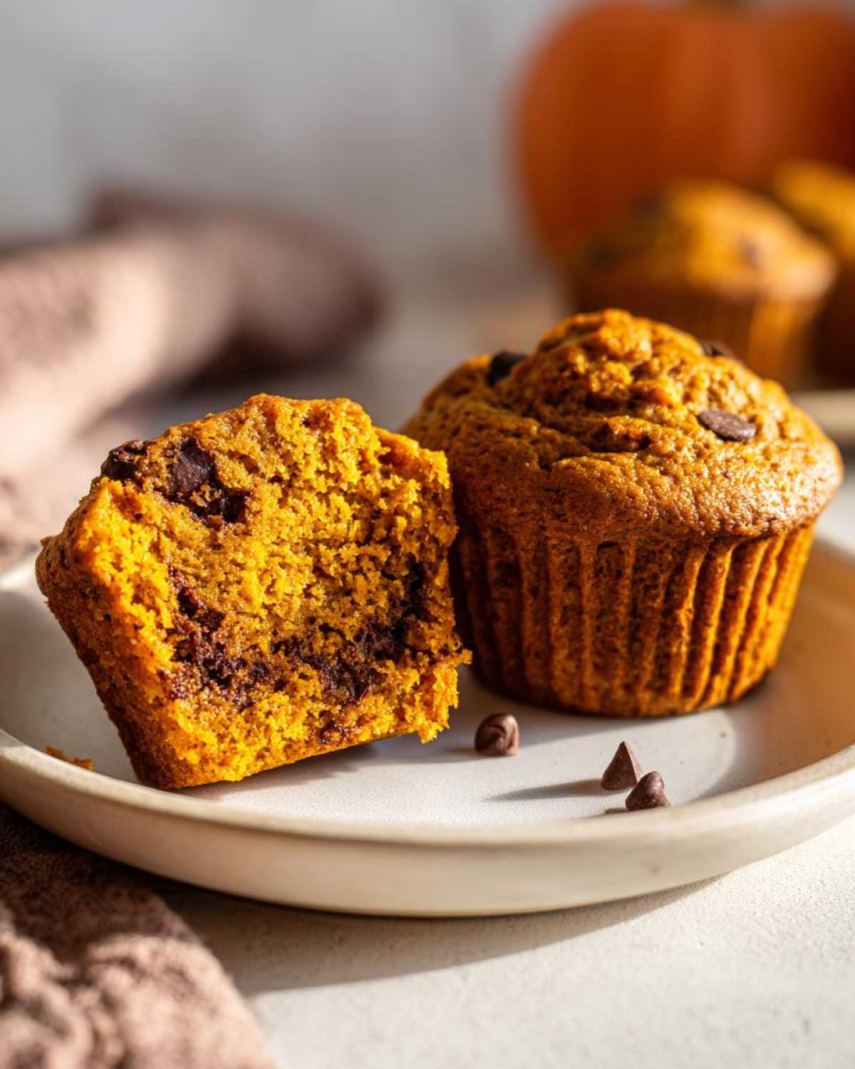 Close-up of pumpkin banana muffins, one cut in half to show the texture and chocolate chips.