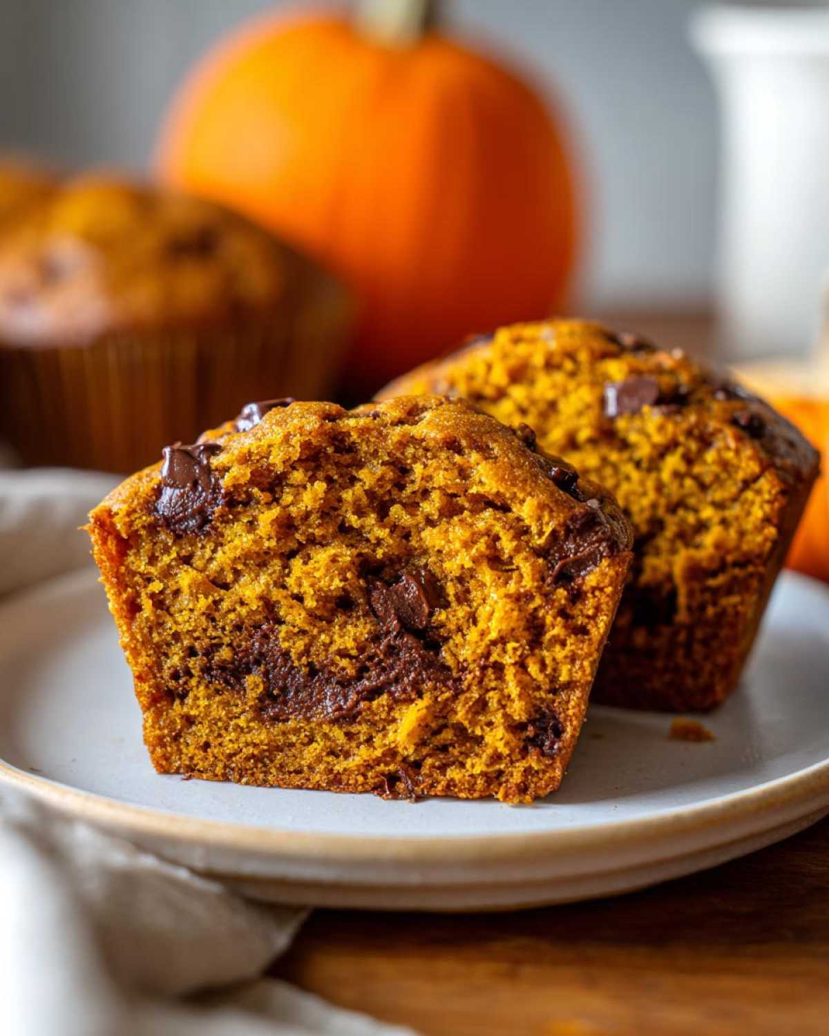 Close-up of pumpkin banana muffins with chocolate chips, one muffin cut in half to show the moist interior.