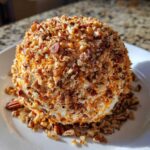 A creamy pumpkin cheese ball coated in chopped pecans, served on a white plate.