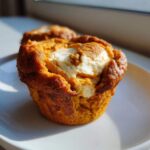 Close-up of a pumpkin cheesecake muffin with a swirl of cream cheese on a white plate.