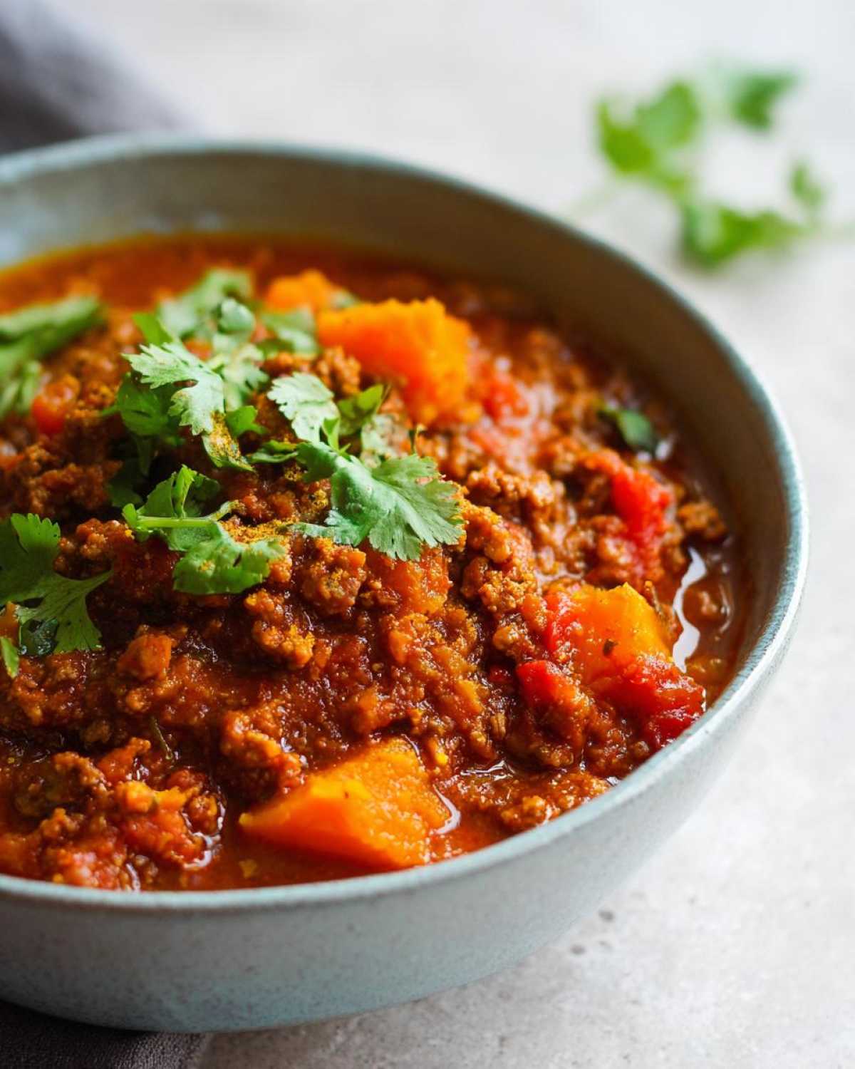 A close-up of a bowl of hearty pumpkin chili, topped with fresh cilantro.