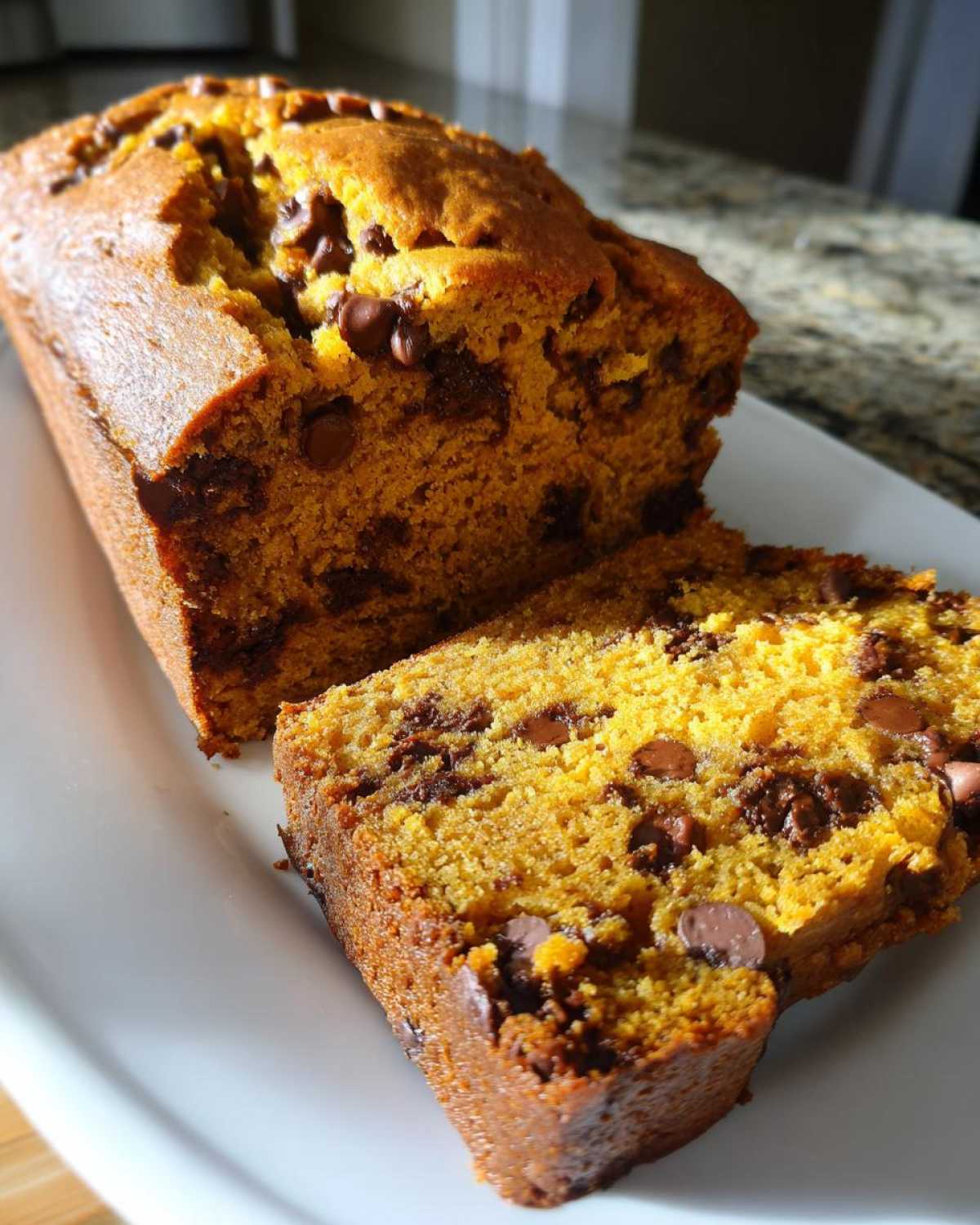 A loaf of pumpkin chocolate chip bread with a slice cut, showcasing the moist texture and chocolate chips.