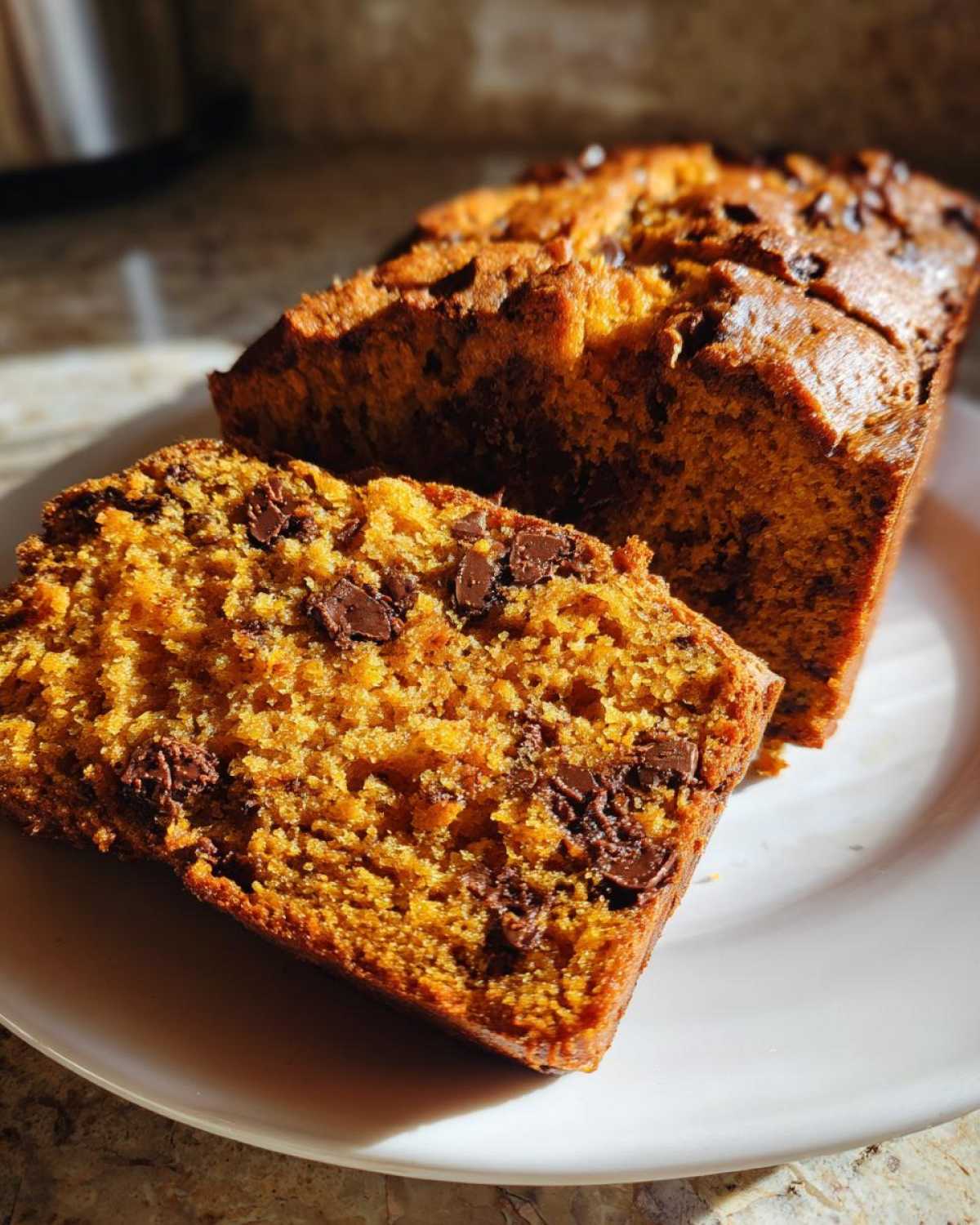 A sliced loaf of pumpkin chocolate chip bread on a white plate, showcasing the moist texture and chocolate chips.