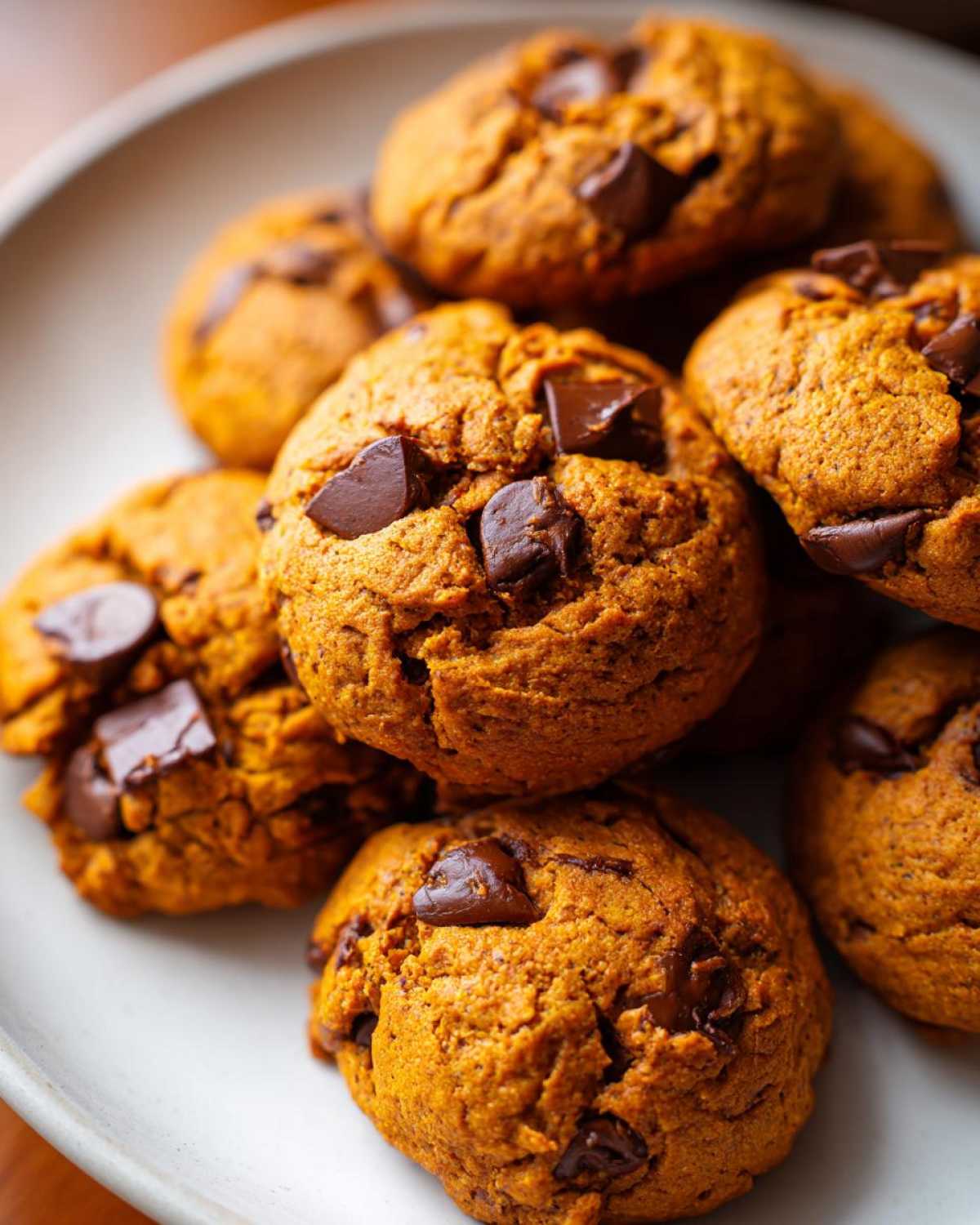 Close-up of a stack of pumpkin chocolate chip cookies on a plate, showcasing their texture and chocolate chunks.