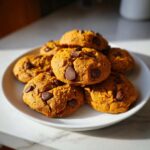 A plate of freshly baked pumpkin chocolate chip cookies, golden brown with melted chocolate chips.