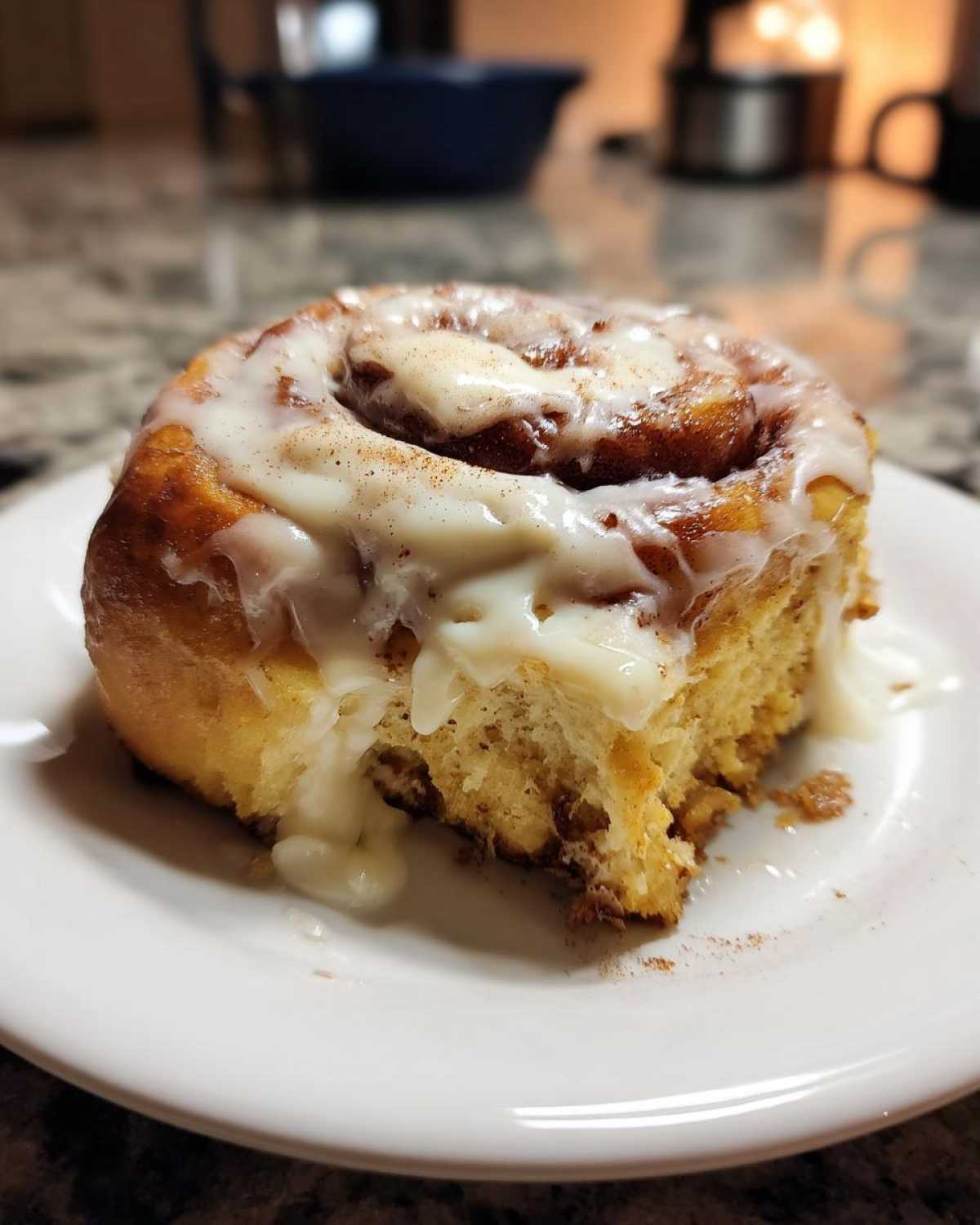 Single iced pumpkin cinnamon roll on a white plate, showing the soft interior and cinnamon filling.