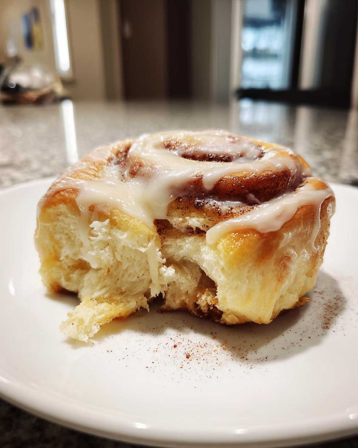 A single, glazed pumpkin cinnamon roll with a bite taken out, sitting on a white plate.