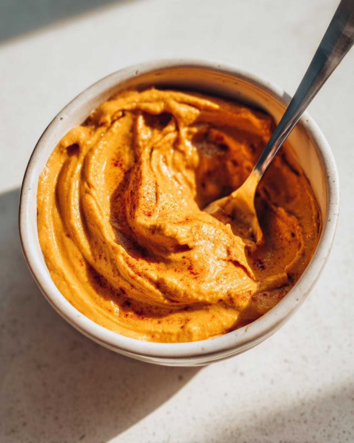 Close-up of pumpkin cream cheese in a white bowl with a spoon, ready to be enjoyed.