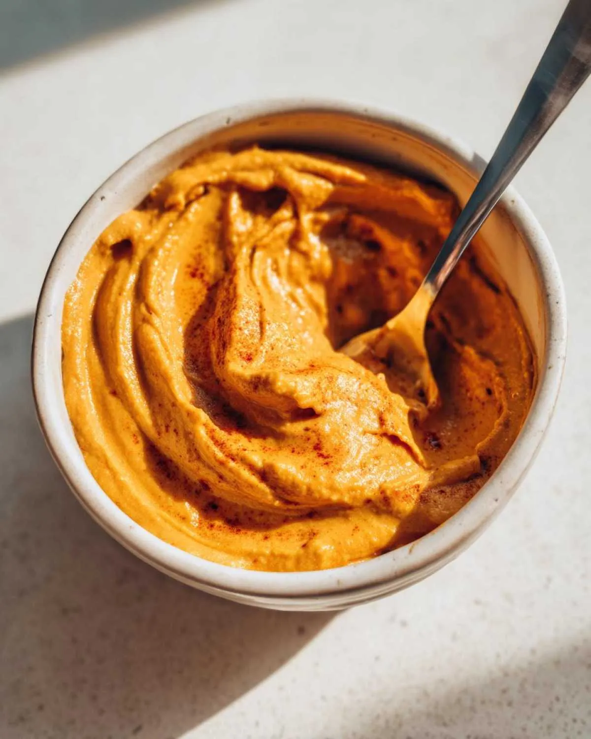 Close-up of pumpkin cream cheese in a white bowl with a spoon, ready to be enjoyed.