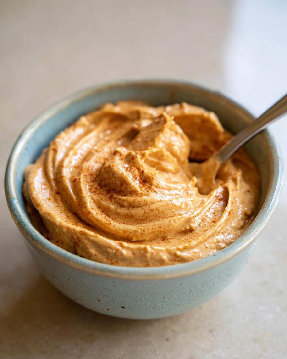 Close-up of a bowl filled with homemade pumpkin cream cheese, topped with a sprinkle of spice.
