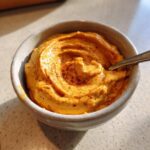 A bowl of creamy pumpkin cream cheese dip, sprinkled with spice, ready to eat with a spoon.