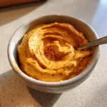 A bowl of creamy pumpkin cream cheese dip, sprinkled with spice, ready to eat with a spoon.