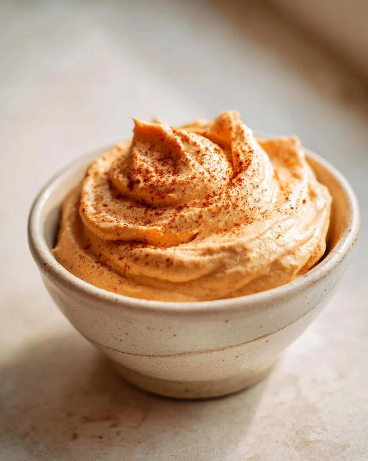 A close-up of fluffy pumpkin fluff dip in a bowl, topped with a sprinkle of cinnamon.