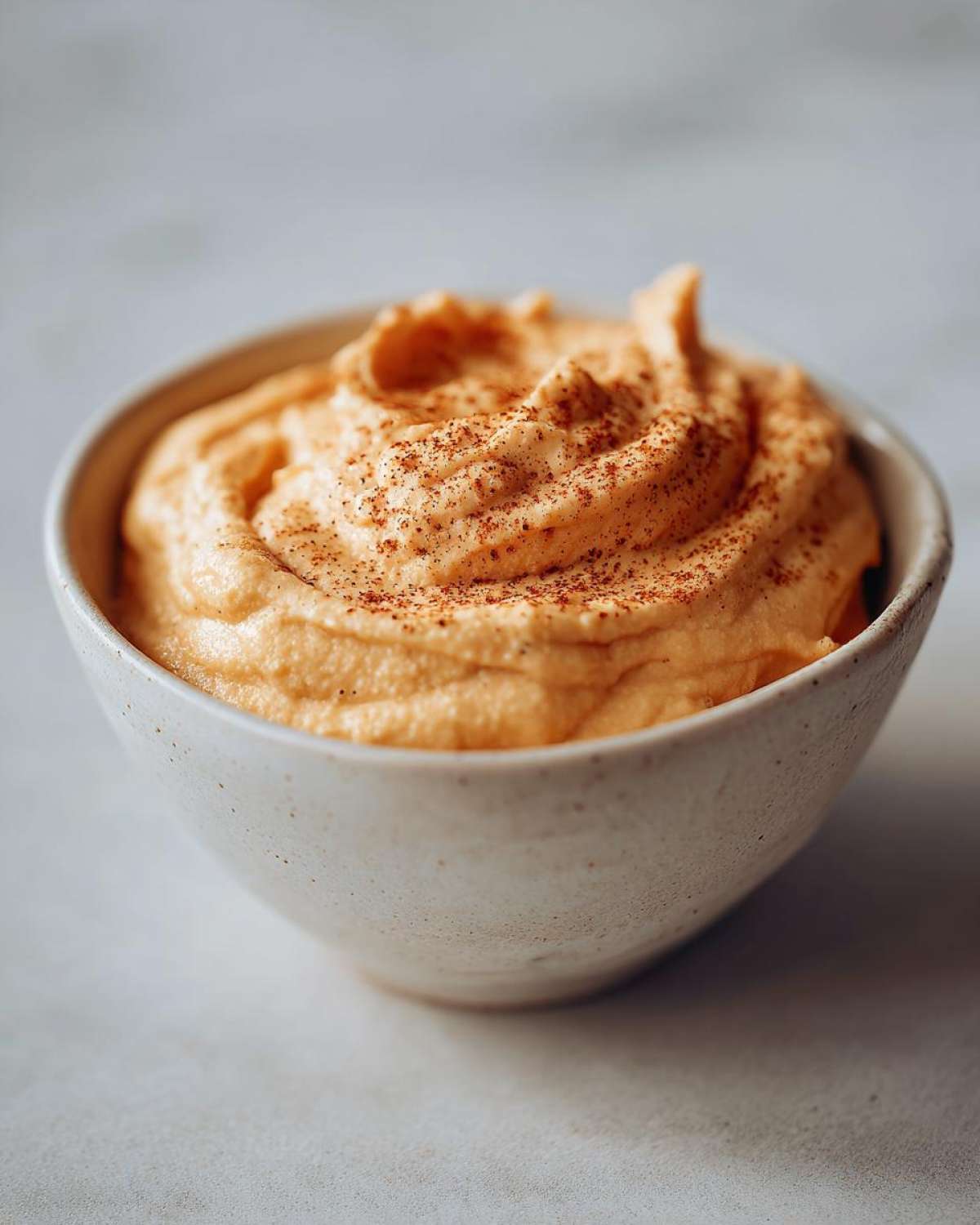A close-up of a bowl filled with creamy pumpkin fluff dip, lightly sprinkled with cinnamon.
