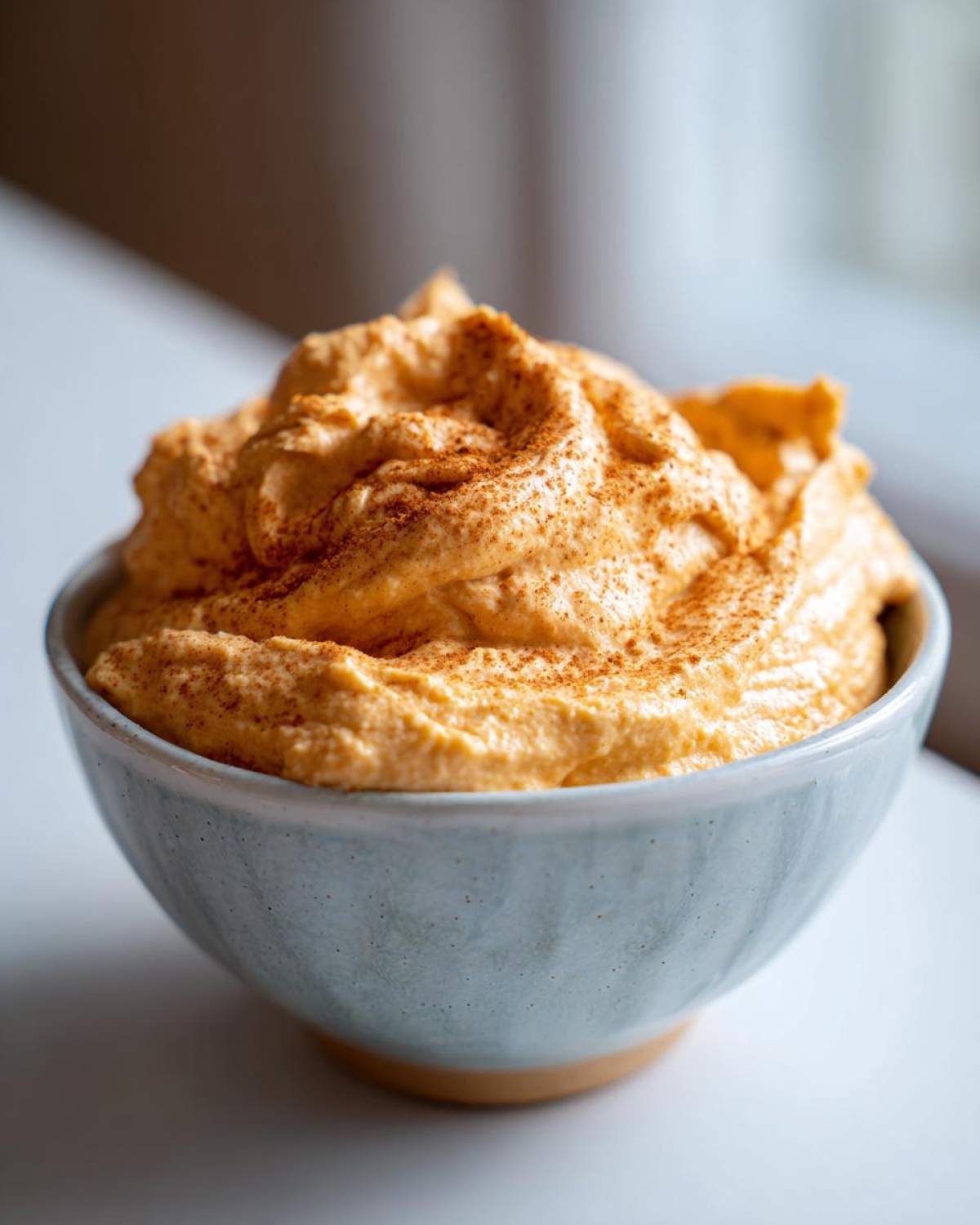 A close-up of a light blue bowl filled with fluffy pumpkin fluff dip, sprinkled with cinnamon.