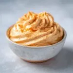 A close-up of a bowl filled with creamy pumpkin fluff dip, swirled and dusted with cinnamon.