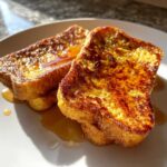 Two slices of golden-brown pumpkin french toast drizzled with syrup on a white plate, ready to eat.