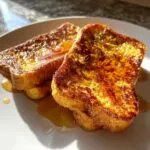 Two slices of golden-brown pumpkin french toast drizzled with syrup on a white plate, ready to eat.