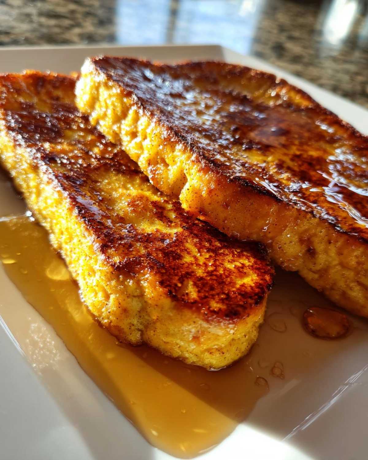 Two slices of golden brown pumpkin french toast drizzled with syrup on a white plate.