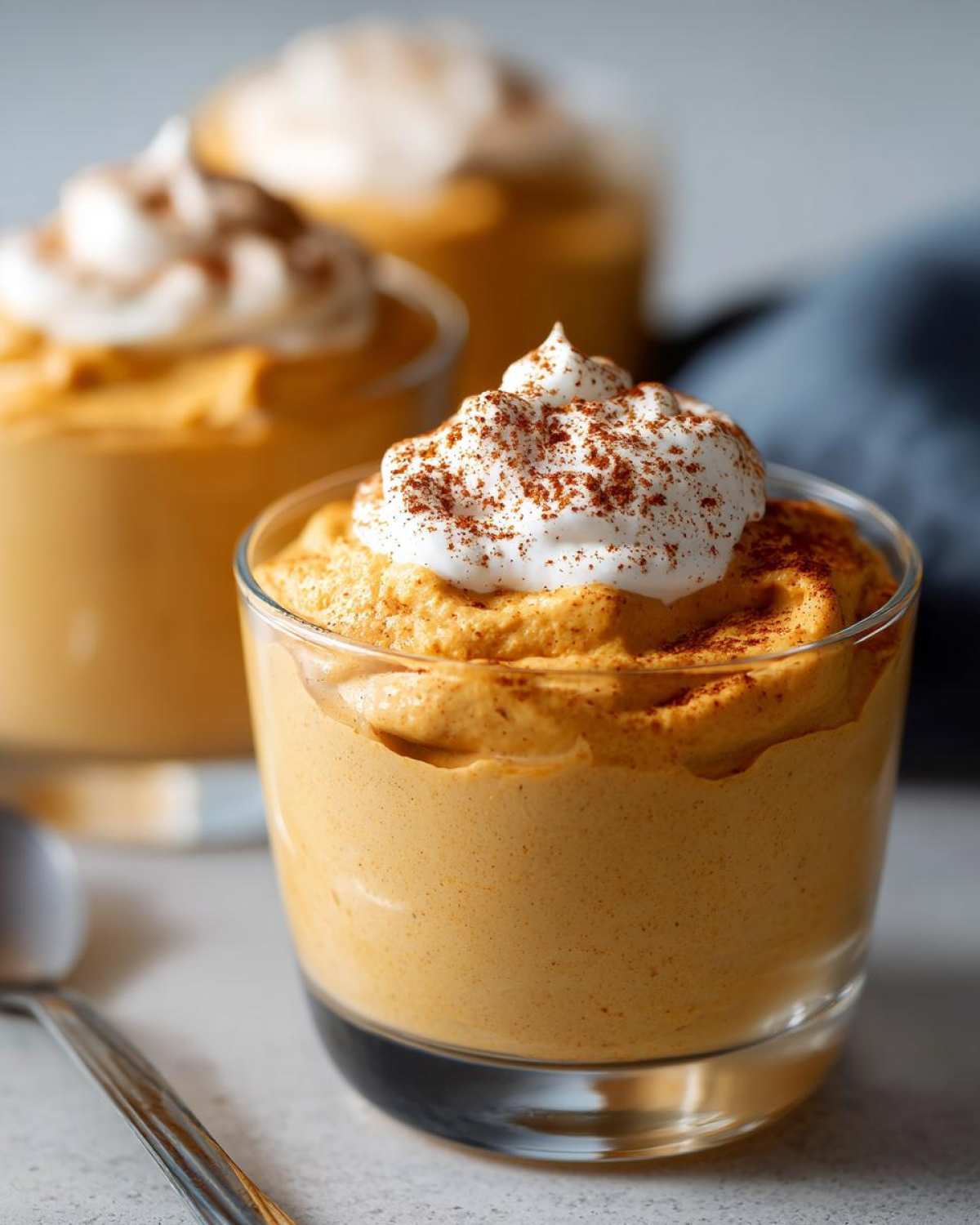 Close-up of a glass of creamy pumpkin mousse topped with whipped cream and cinnamon.