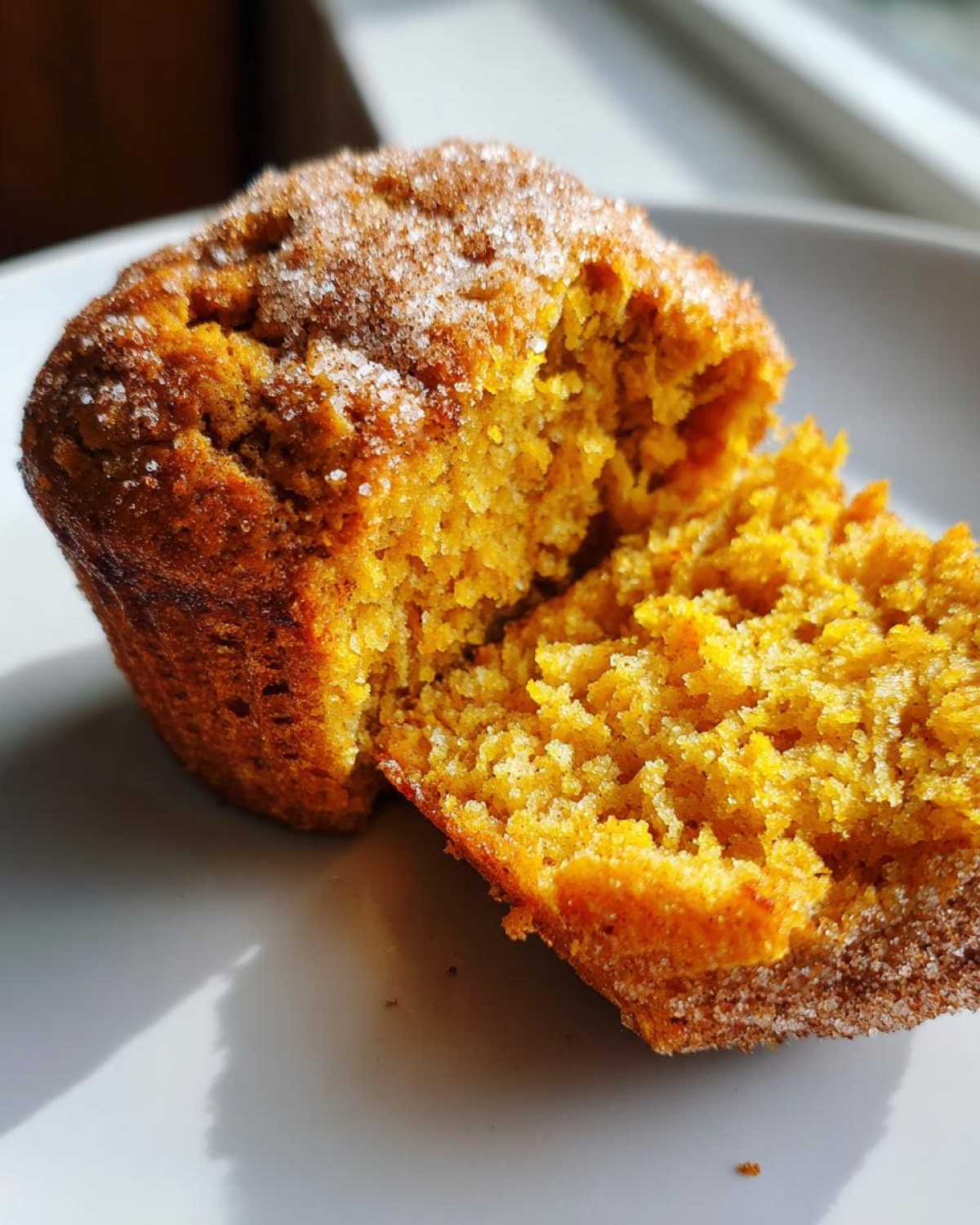Close-up of a moist pumpkin muffin, split open to show the texture, topped with sugar.