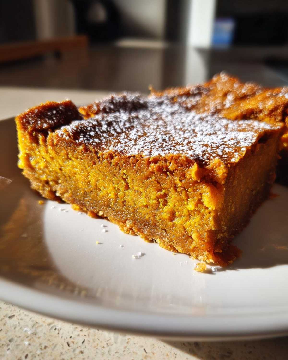 Close-up of a slice of pumpkin pie bars, dusted with powdered sugar on a white plate.