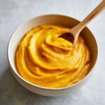 A close-up of velvety pumpkin puree in a bowl with a wooden spoon.