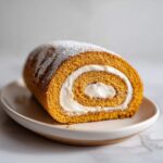 A close-up of a delicious pumpkin roll with cream filling, dusted with powdered sugar.