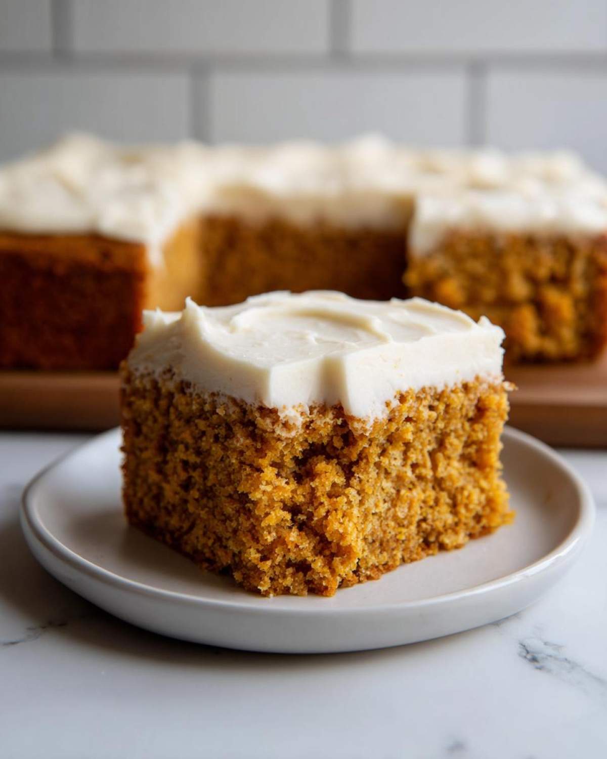 A close-up of a moist slice of pumpkin sheet cake with creamy white frosting.