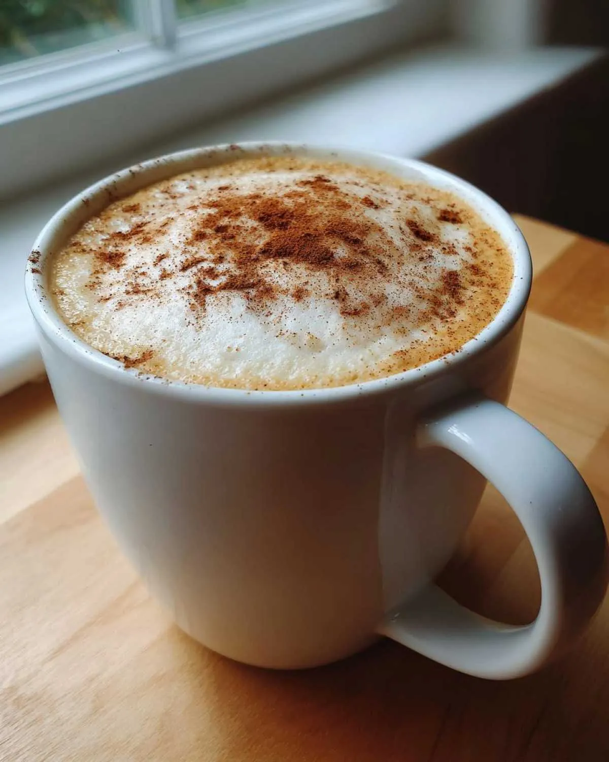 A creamy pumpkin spice latte in a white mug, topped with foam and a sprinkle of pumpkin spice.