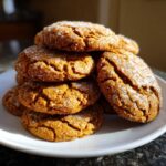 A stack of homemade pumpkin sugar cookies, glazed with sugar, on a white plate.