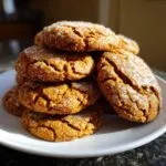 A stack of homemade pumpkin sugar cookies, glazed with sugar, on a white plate.