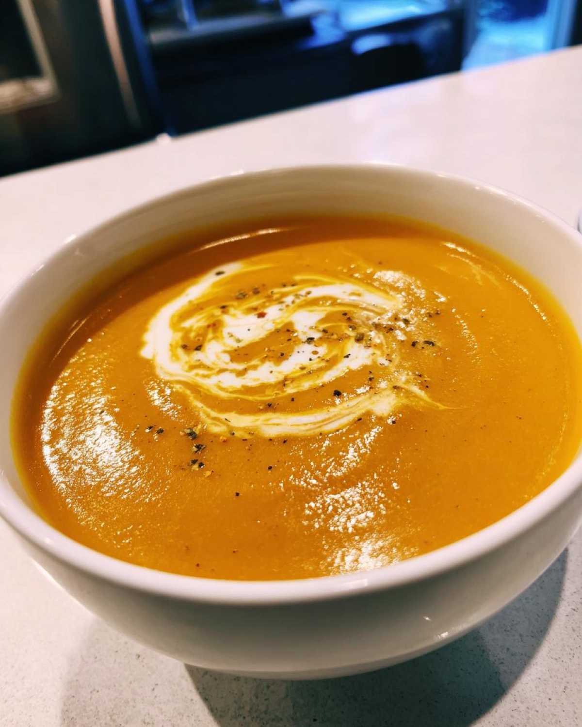 A bowl of creamy roasted butternut squash soup, swirled with cream and sprinkled with pepper.